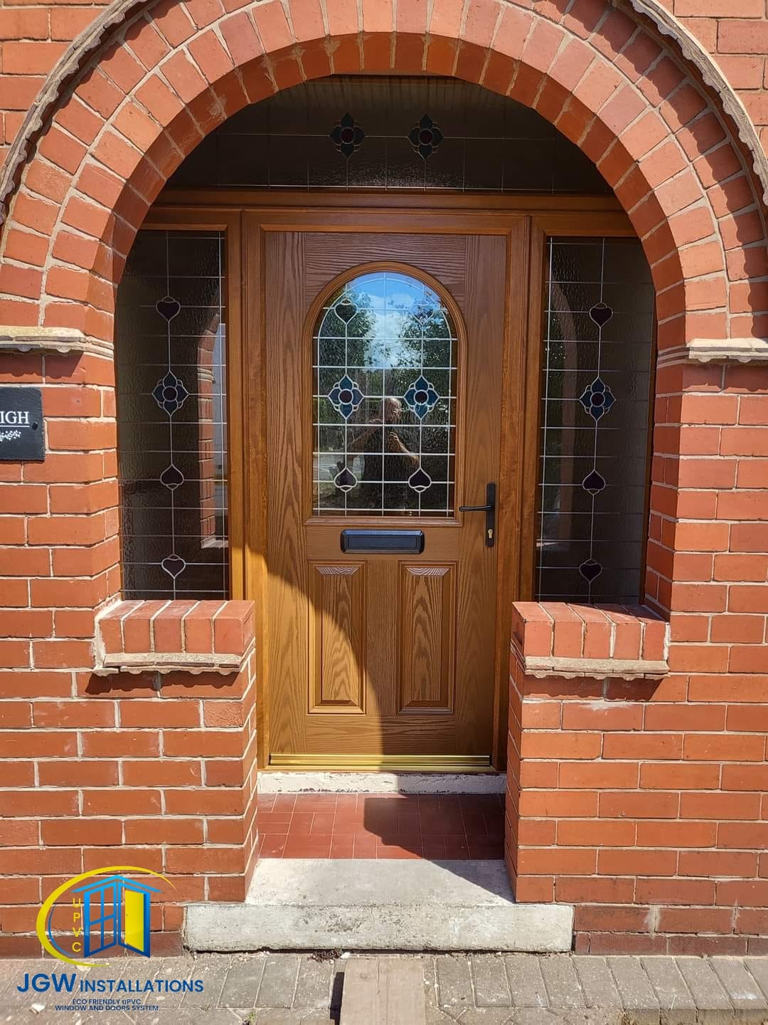 Golden oak composite front door with decorative leaded side lights in brick arch