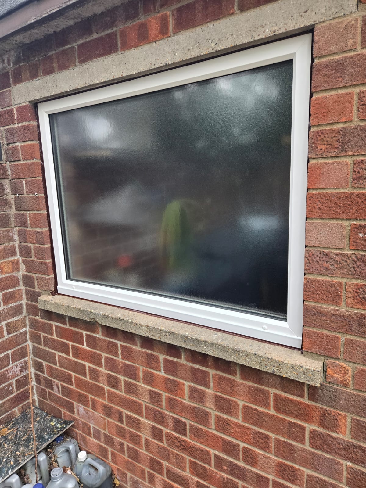 White uPVC fixed window with obscure glazing fitted in a red brick wall above a concrete sill