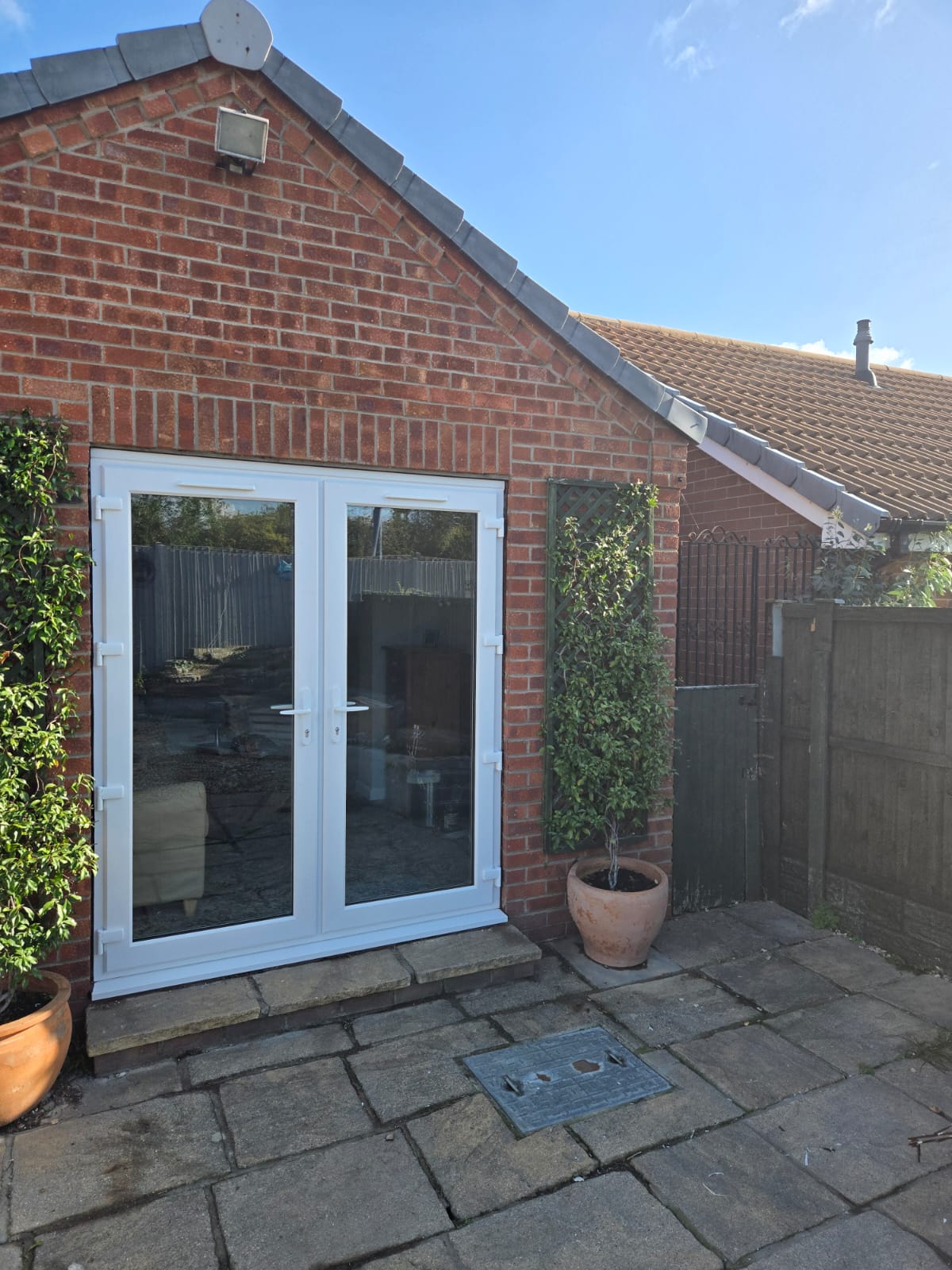 White uPVC French doors fitted in the gable end of a red brick garden room opening onto a stone patio
